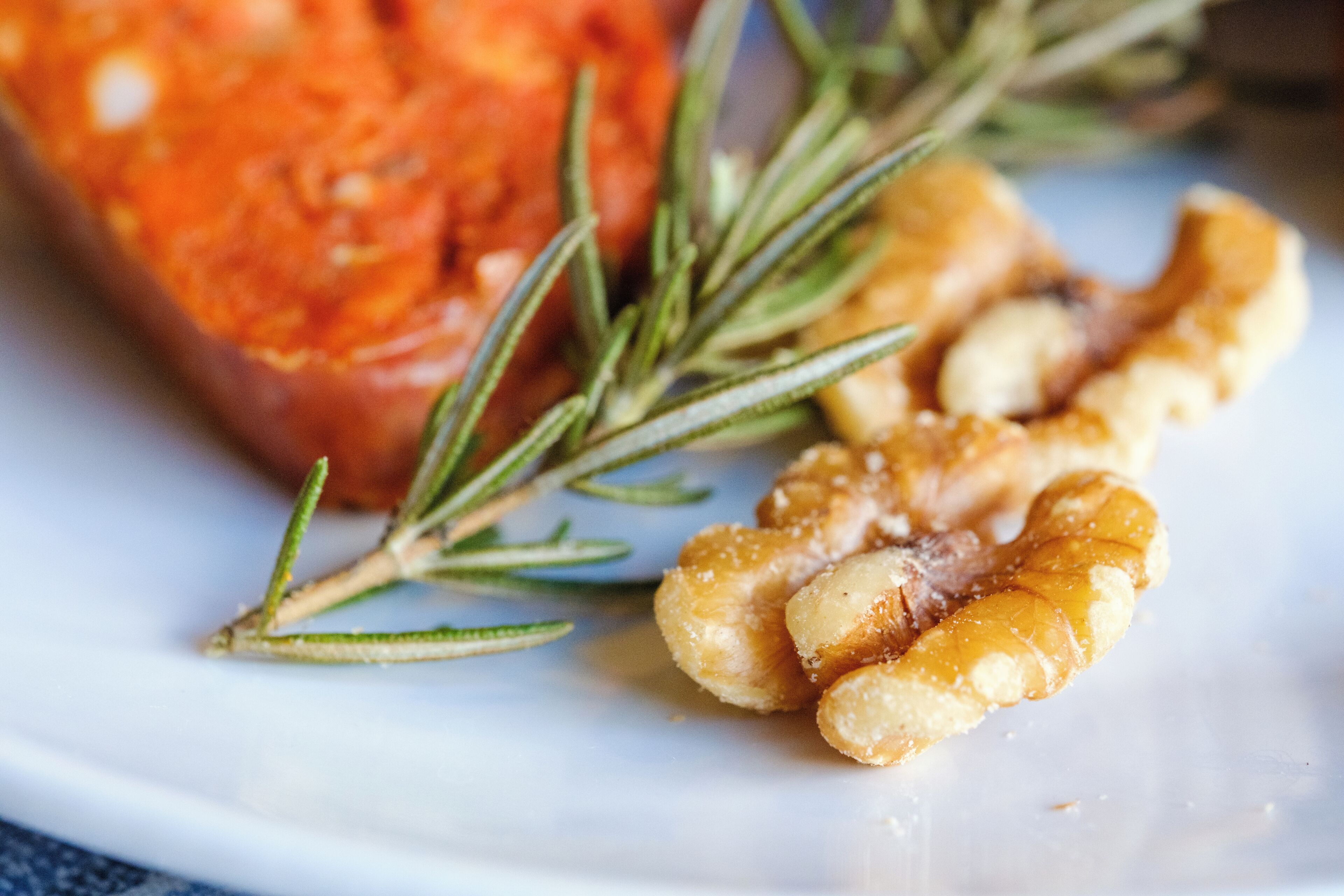 A plate with roasted nuts and a sprig of rosemary.