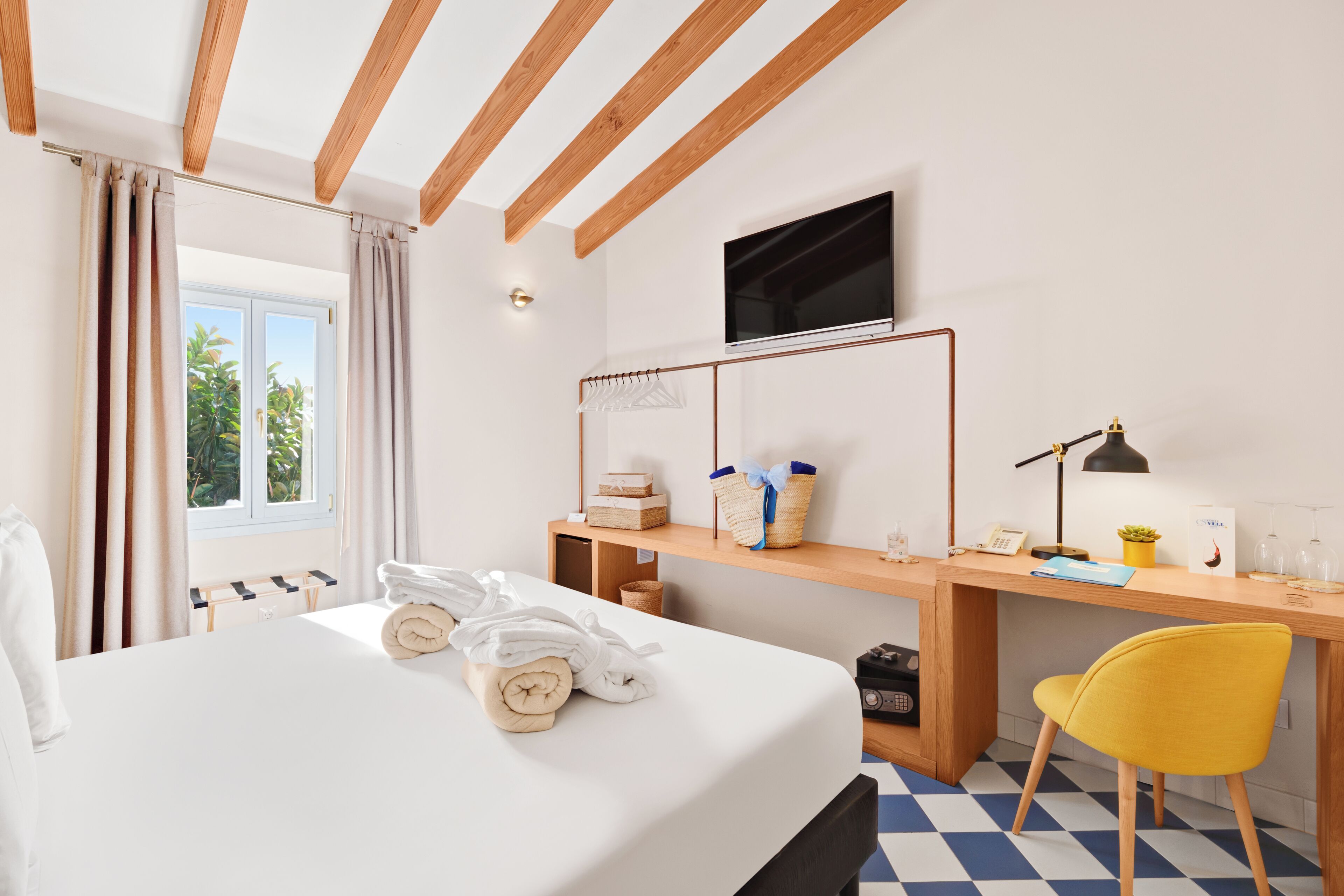 A hotel room with a bed, a desk, a chair, a TV, and a window with curtains.