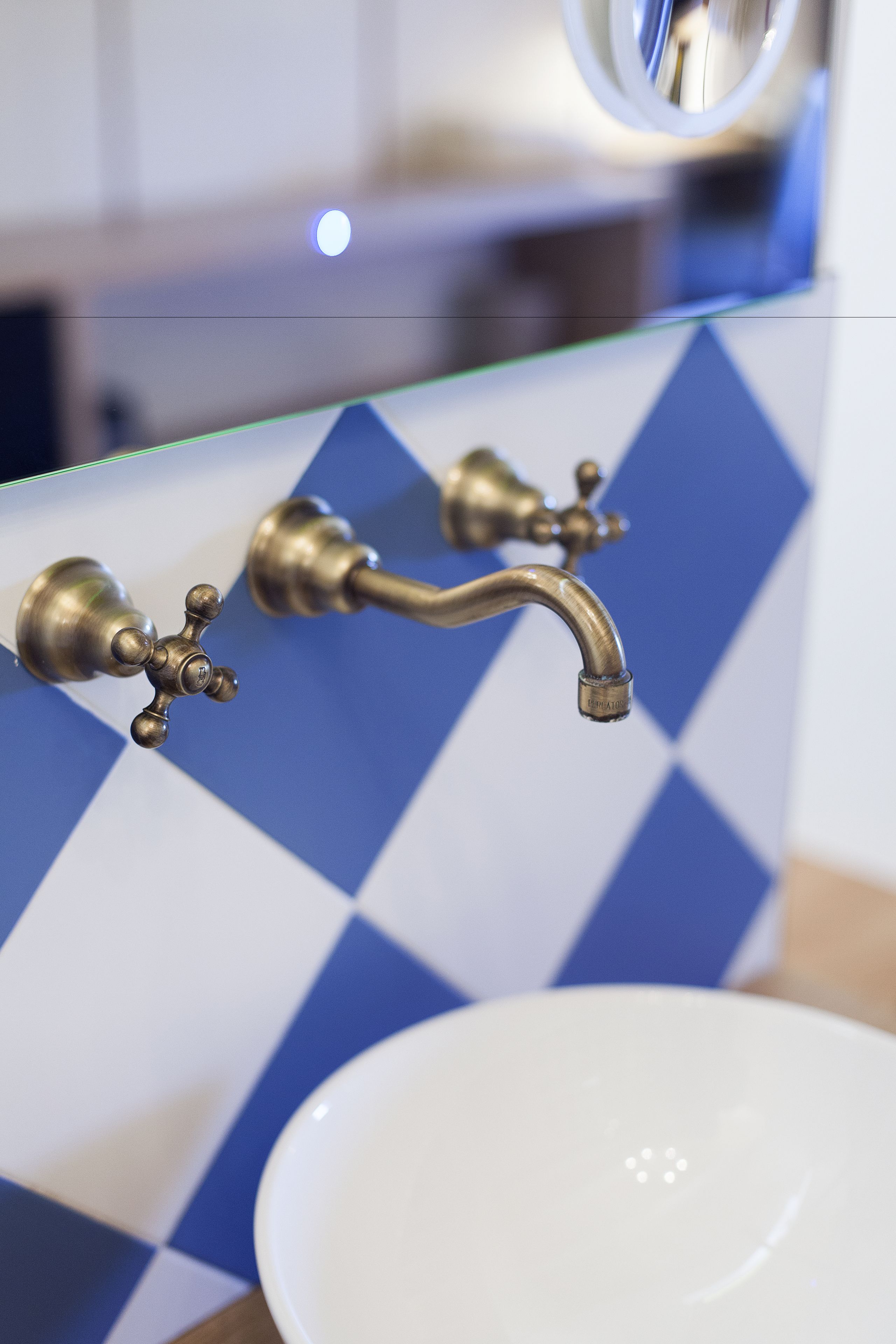 Casa de banho com lavatório branco, torneira de latão e painel de azulejos quadriculado azul e branco.