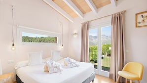 A bedroom with a large bed, a window with a view of greenery, a balcony with a chair, and a wooden ceiling. - Es Corte Vell - Inland Bunyola - Adults Only (Bunyola)