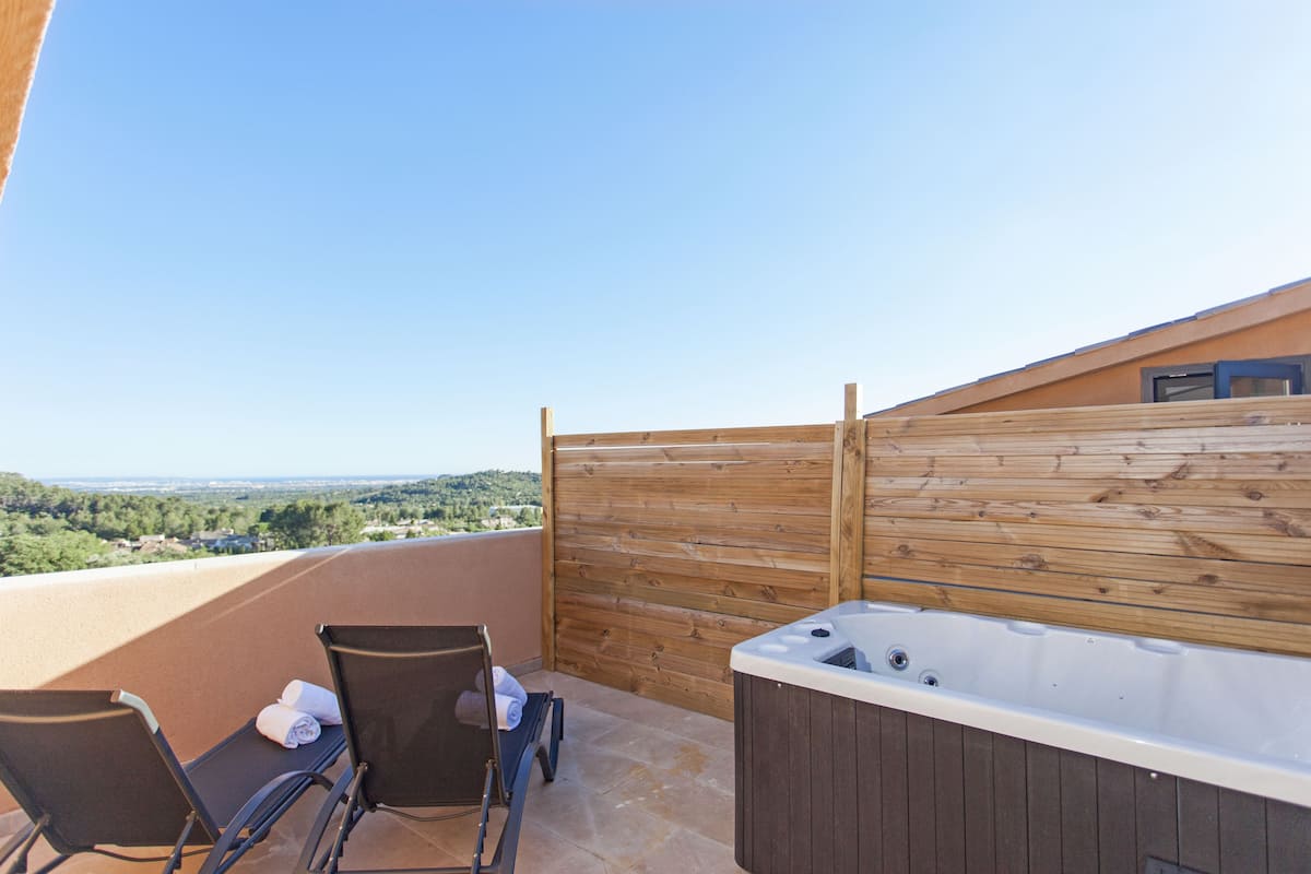 A balcony with a hot tub, two chairs, and a wooden fence.