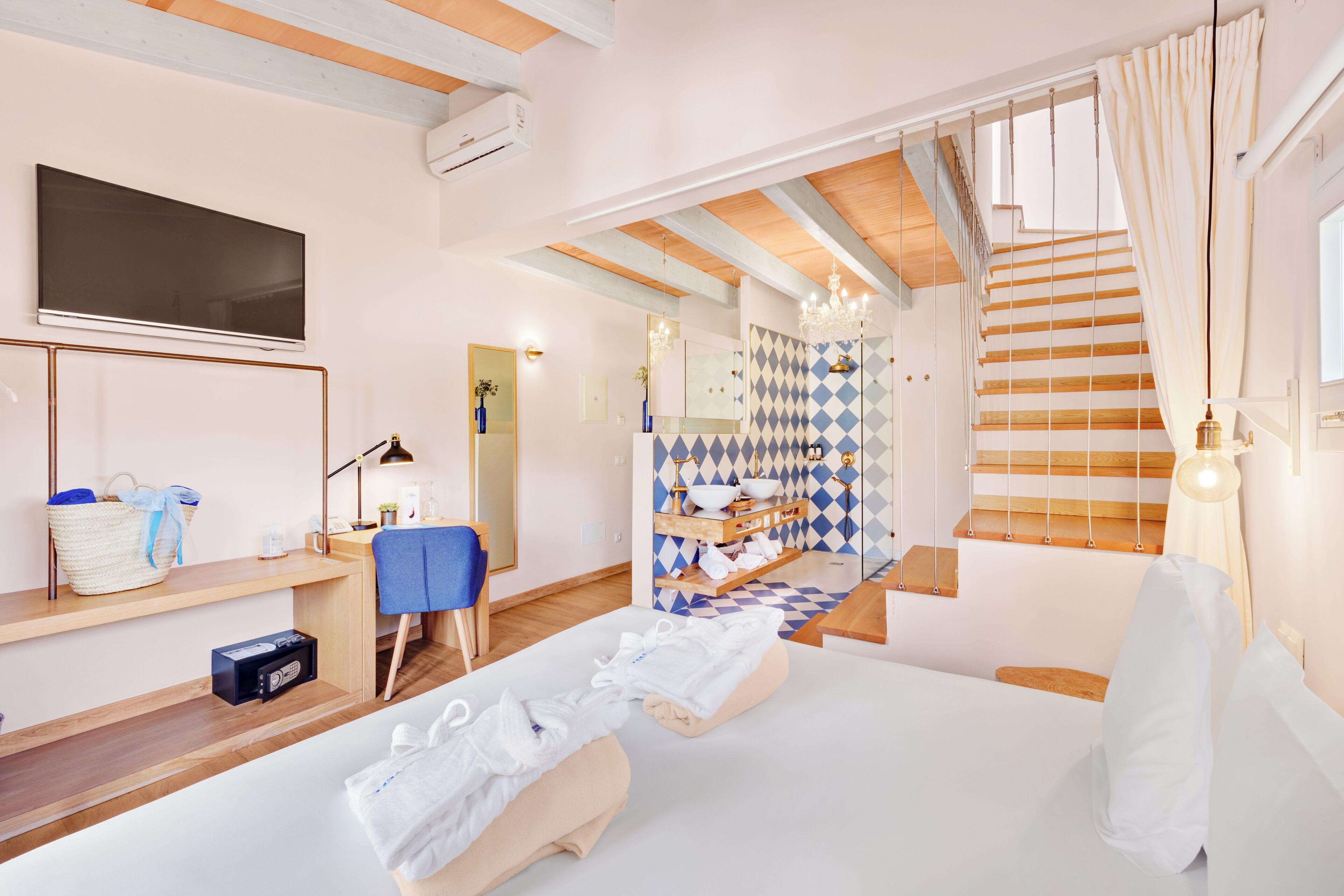 Una habitación de hotel con cama, escritorio, televisor y baño con salpicadero de azulejos geométricos.