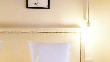 Habitación de hotel con una cama bien hecha, ropa blanca, una obra de arte enmarcada en la pared y una lámpara de noche.