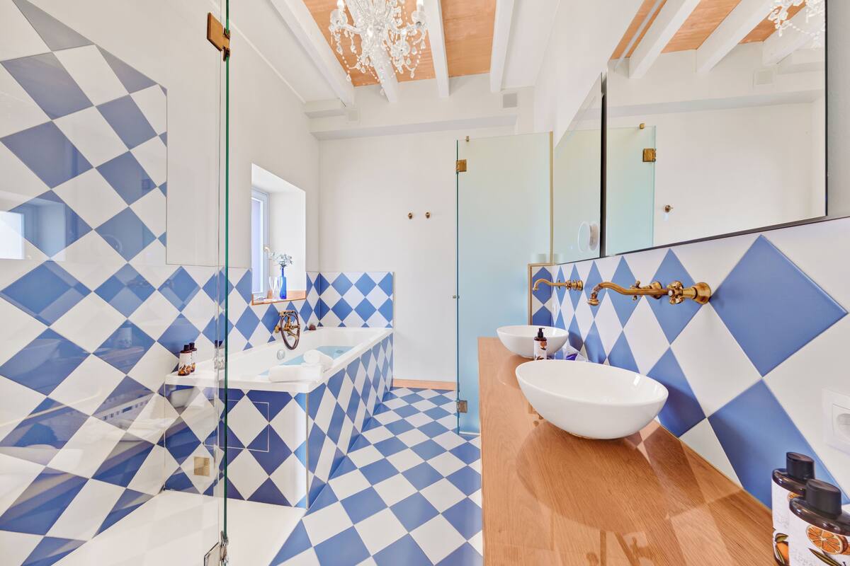A modern bathroom with a geometric tile pattern, a large mirror, and a wooden vanity.