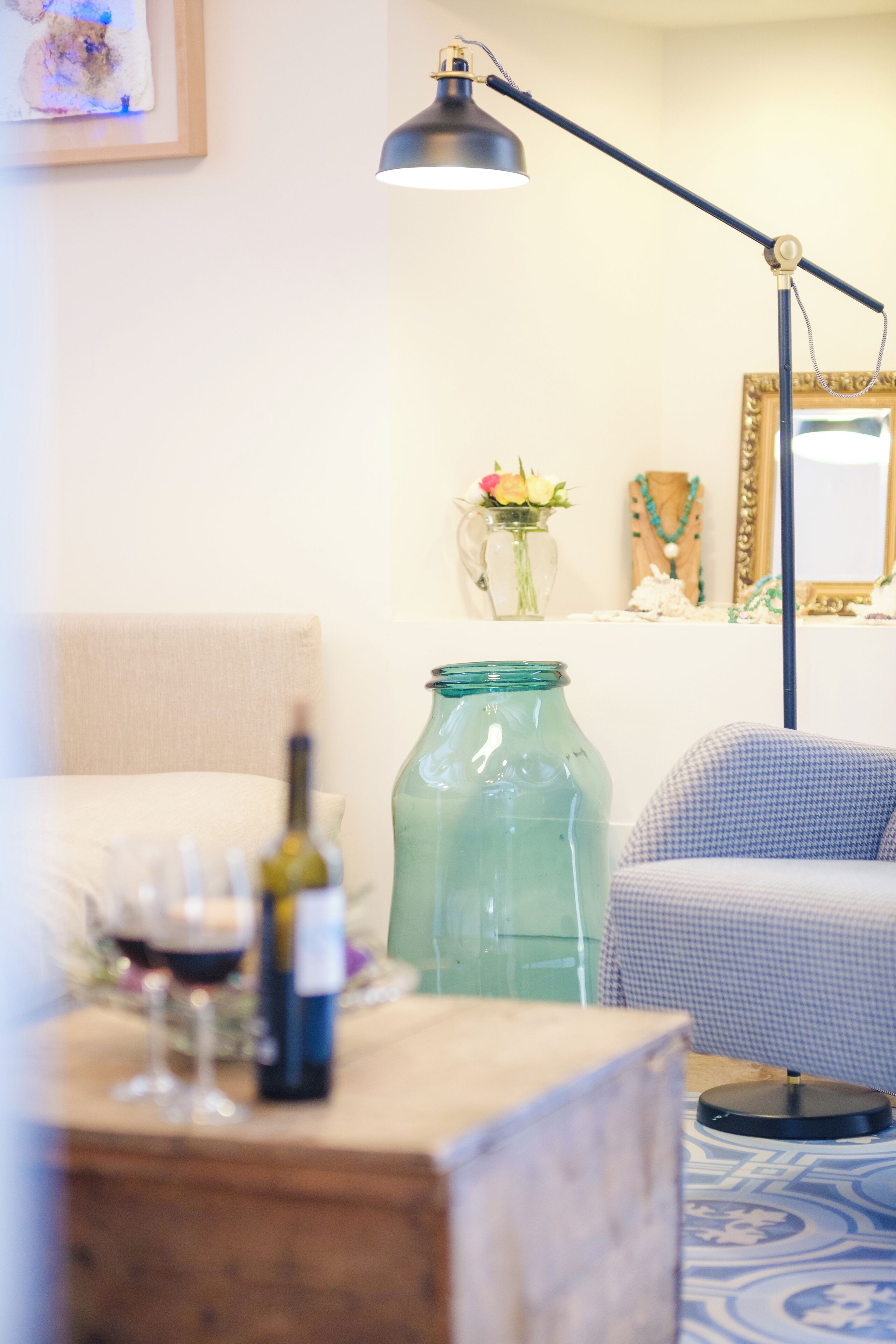 A room with a wooden table, a green glass jar, a wine bottle, and a checkered chair.