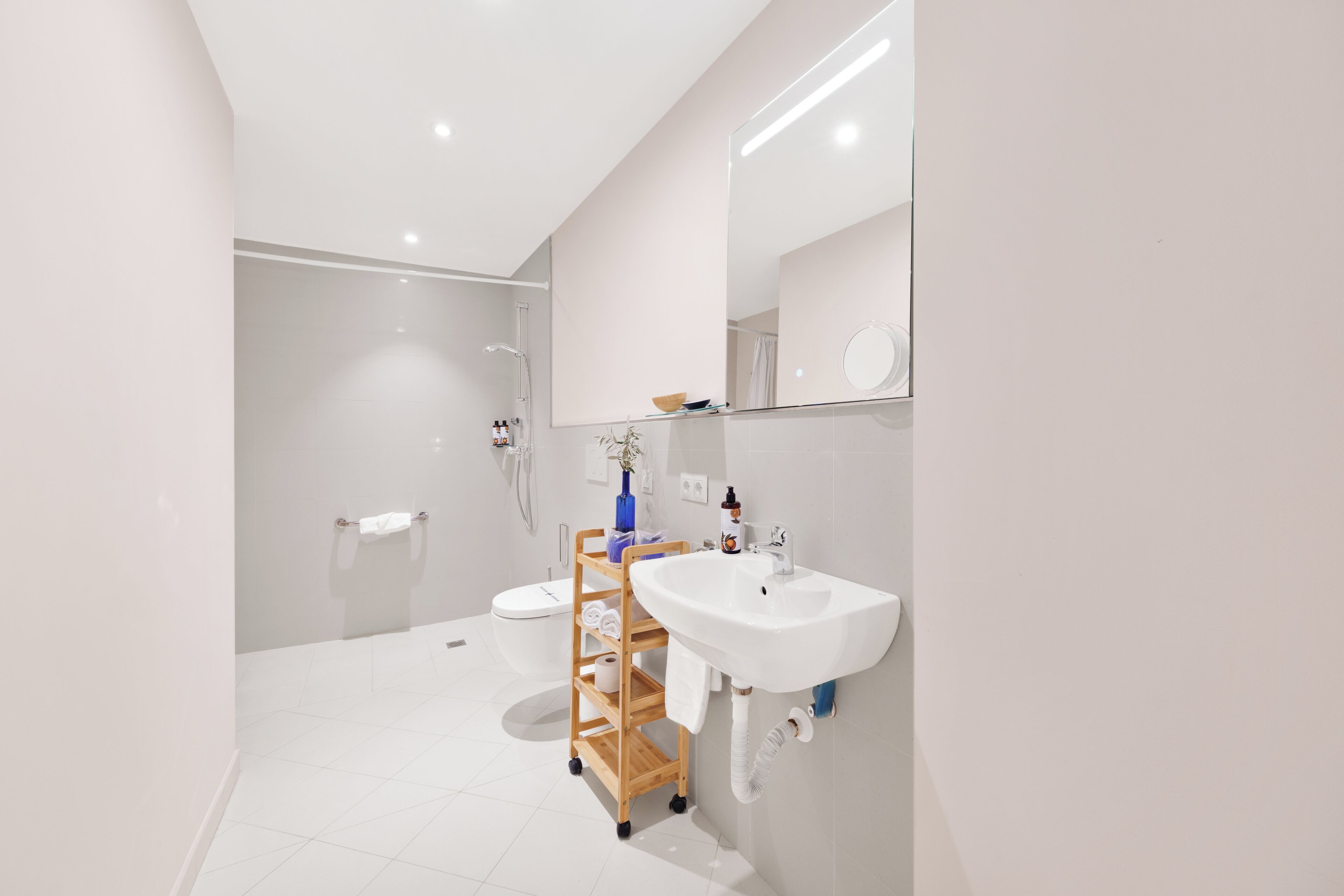 A modern bathroom with a white sink, a mirror, and a wooden shelf unit.