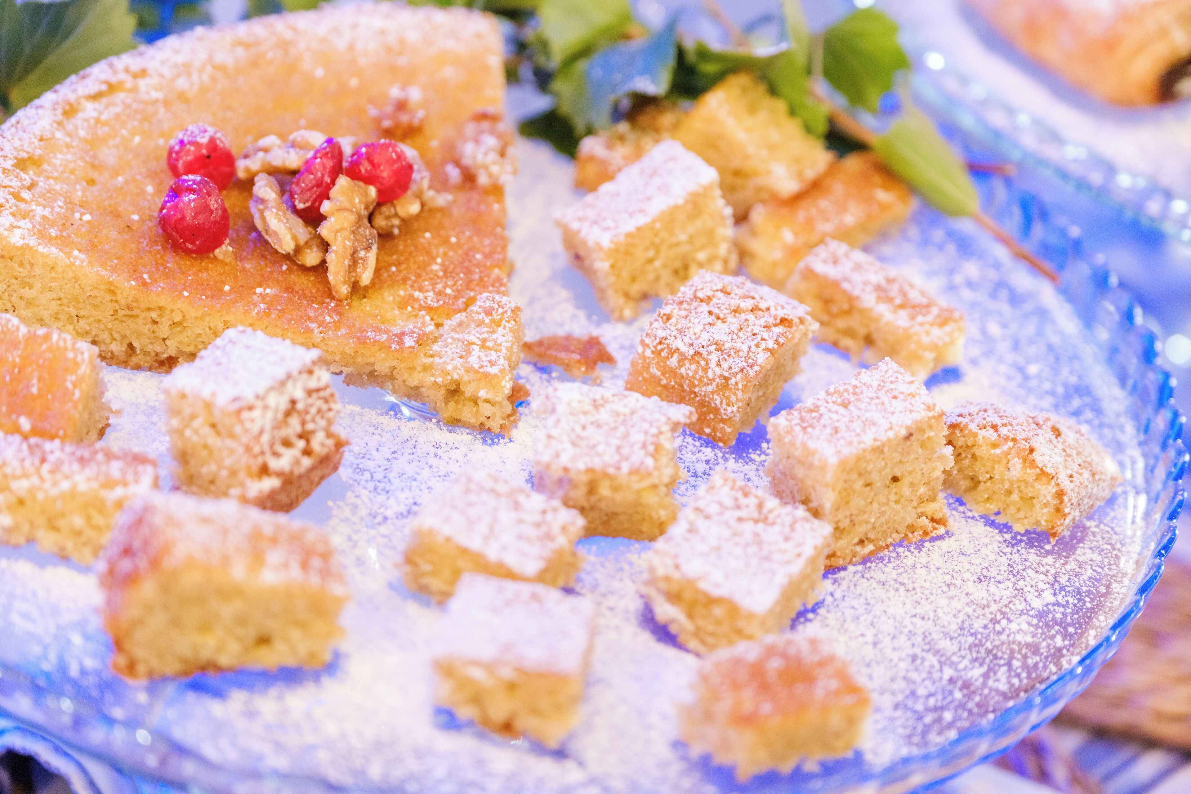 Un plato de postre con una porción de pastel, pequeños trozos cuadrados de pastel y frutos rojos.