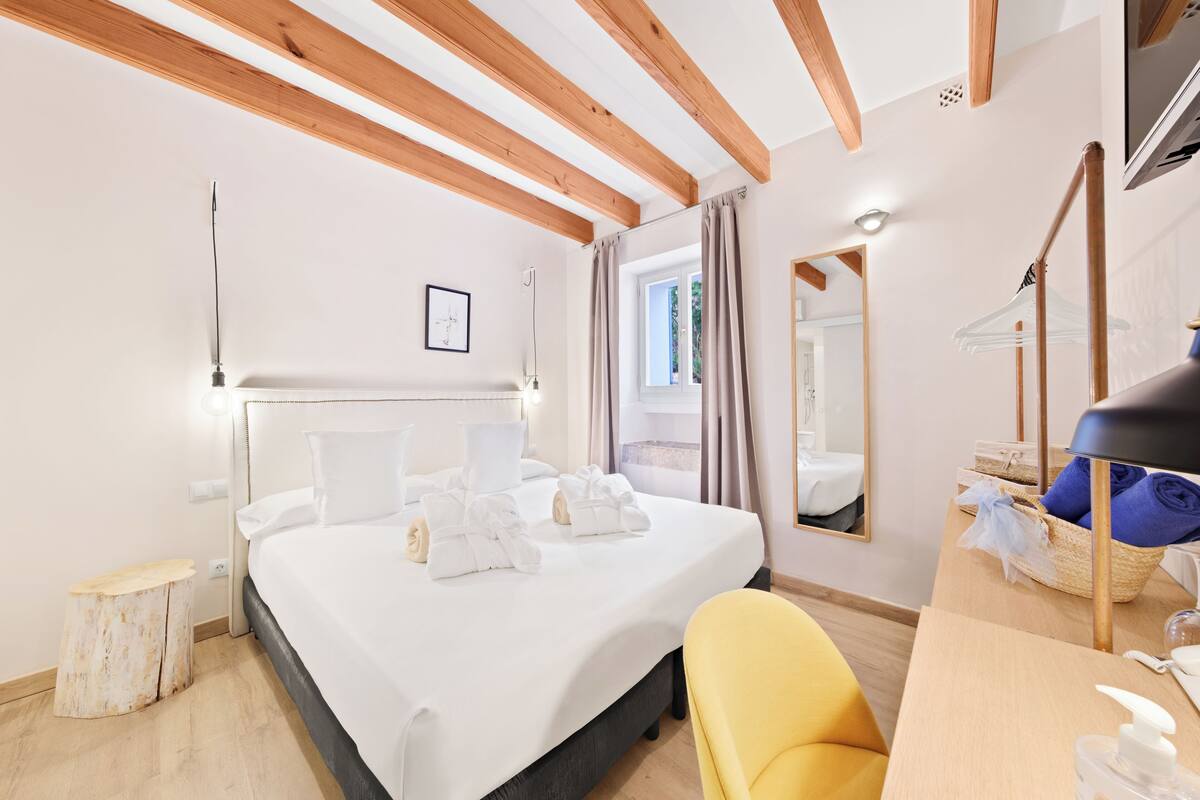 A hotel room with a bed, a wooden headboard, a bedside table with a lamp, a chair, and a mirror.