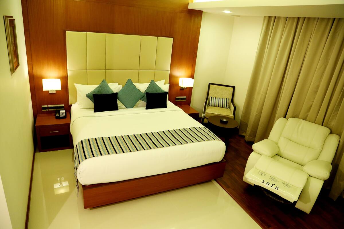 A hotel room with a large bed, two bedside tables with lamps, a sofa, and a chair.