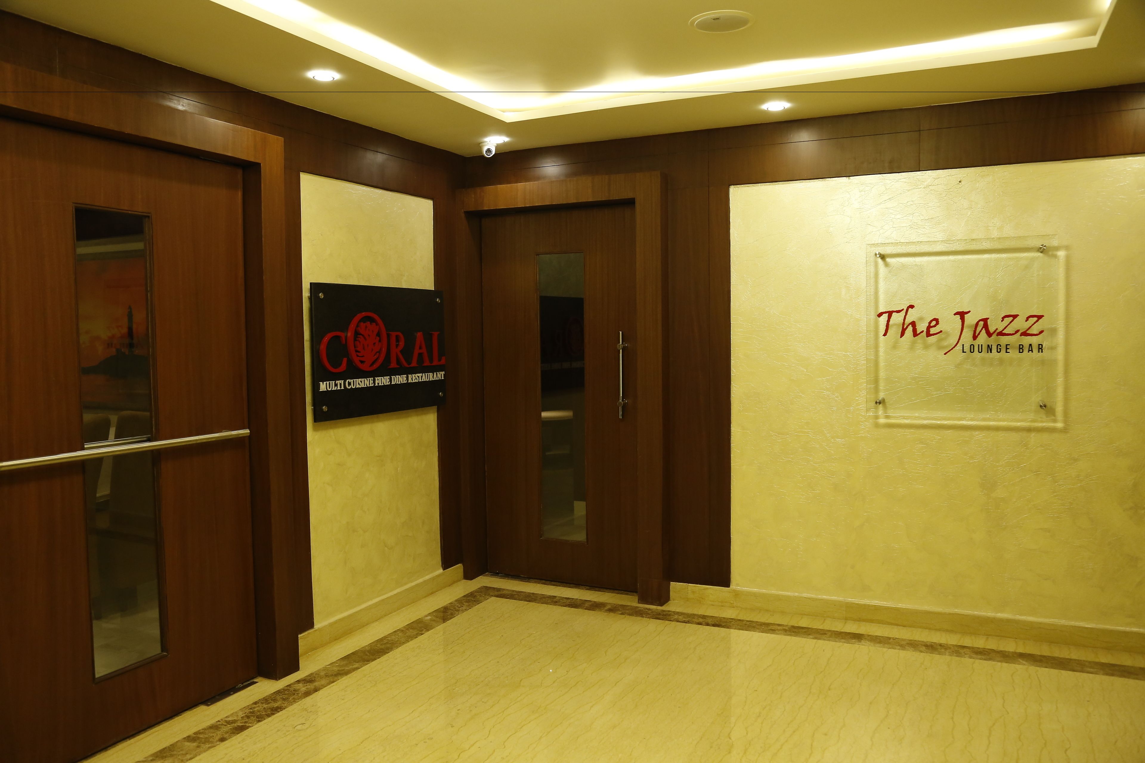 A hallway with wooden doors, a sign for 'CORAL Multi Cuisine Fine Dining Restaurant', and a sign for 'The Jazz Lounge Bar'.