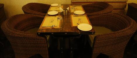 A dining table set for four with wicker chairs, a wooden table, and a menu.
