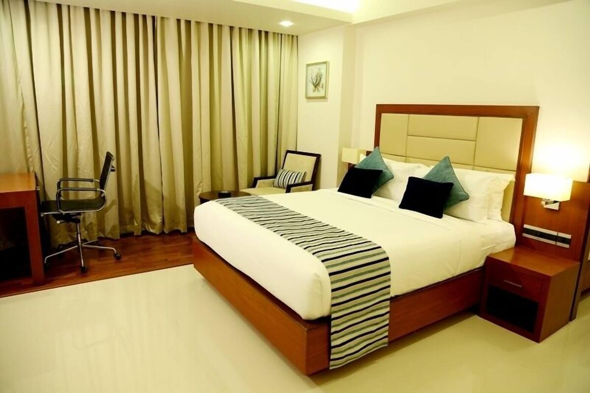 A hotel room with a large bed, a desk, a chair, and a nightstand.