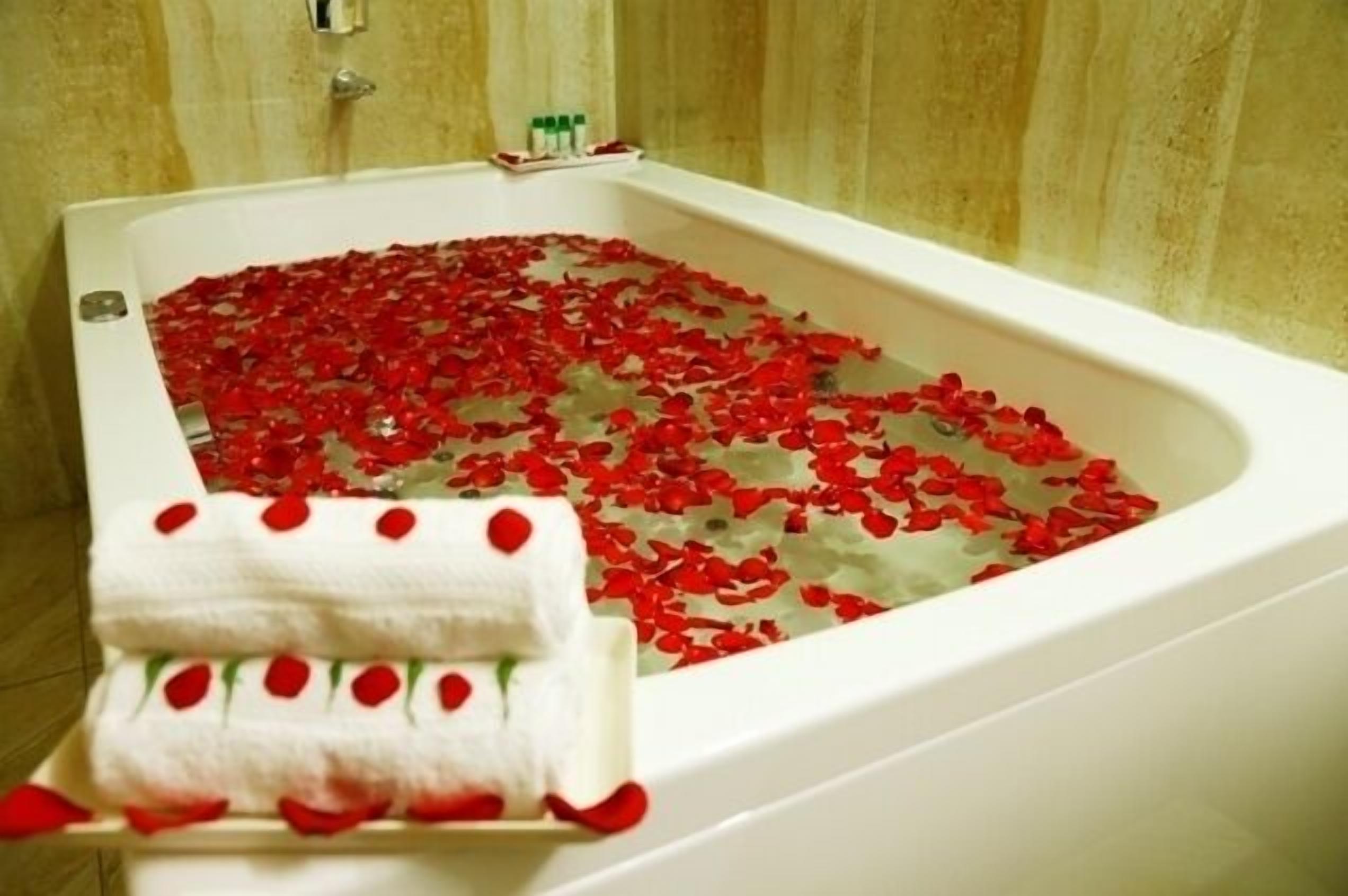 Une baignoire remplie de pétales de rose, une serviette blanche parsemée de pétales de rose et une bouteille de shampoing.
