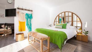A bedroom with a bed, bench, bedside table, lamp, and a TV on a stand. - Suites del Arenal Olehousing (Seville)