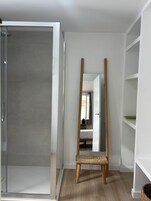 Una habitación con puerta de ducha de vidrio, una silla de madera y un espejo de cuerpo entero.