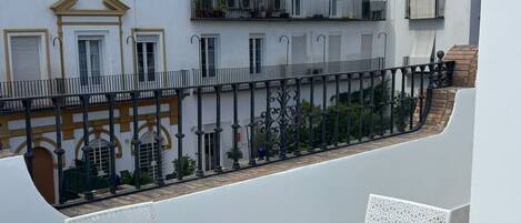 Un balcón con una mesa redonda y cuatro sillas, con vista a un patio con edificios.