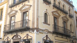 A corner building with a balcony, a door, and a sign. - Suites del Arenal Olehousing (Seville)