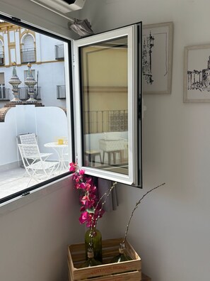 A room with a window, a table, chairs, and a decorative vase with flowers. - Suites del Arenal Olehousing (Seville)