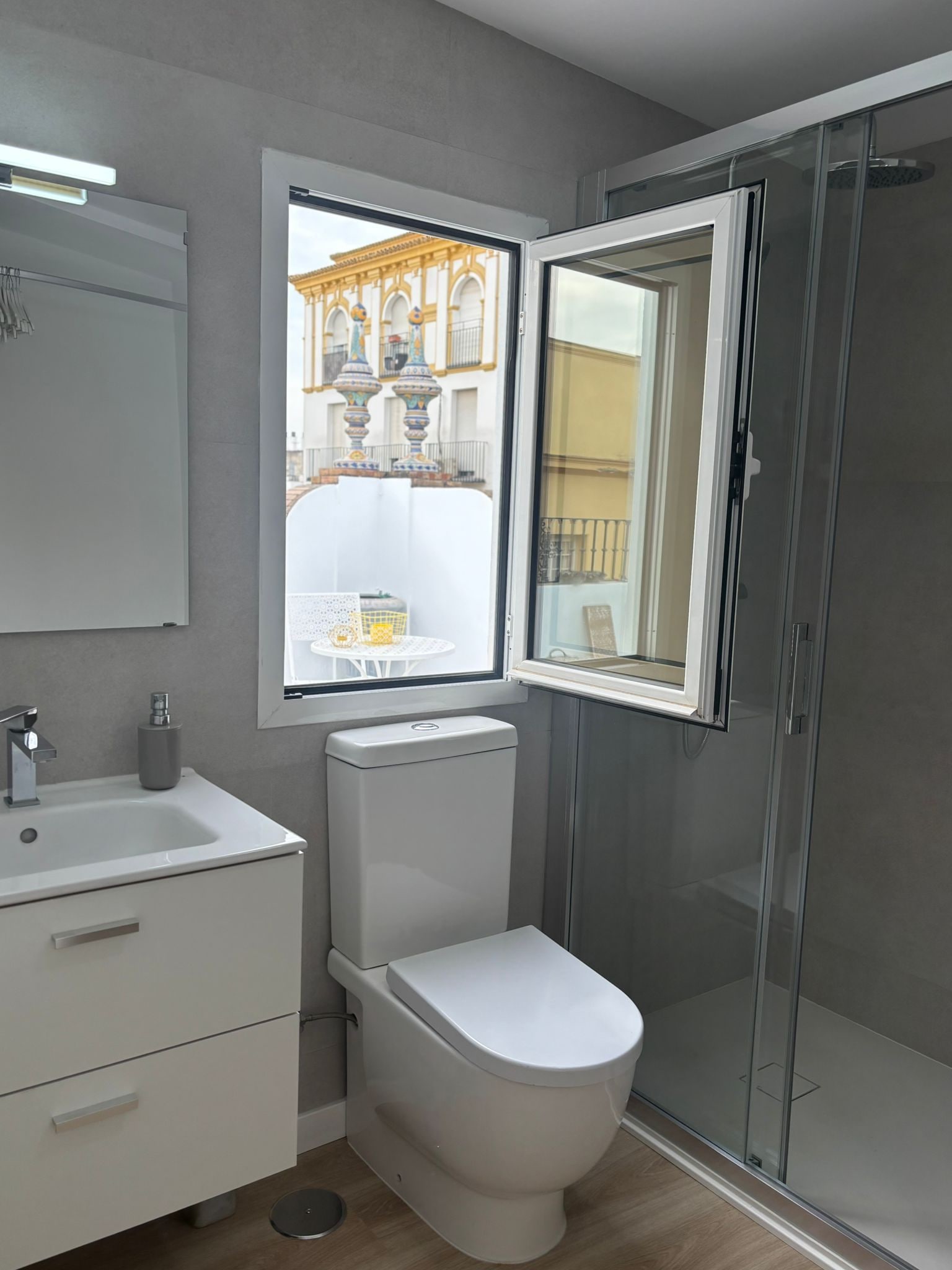 A modern bathroom with a toilet, sink, and a window offering a view of a building with ornate columns.