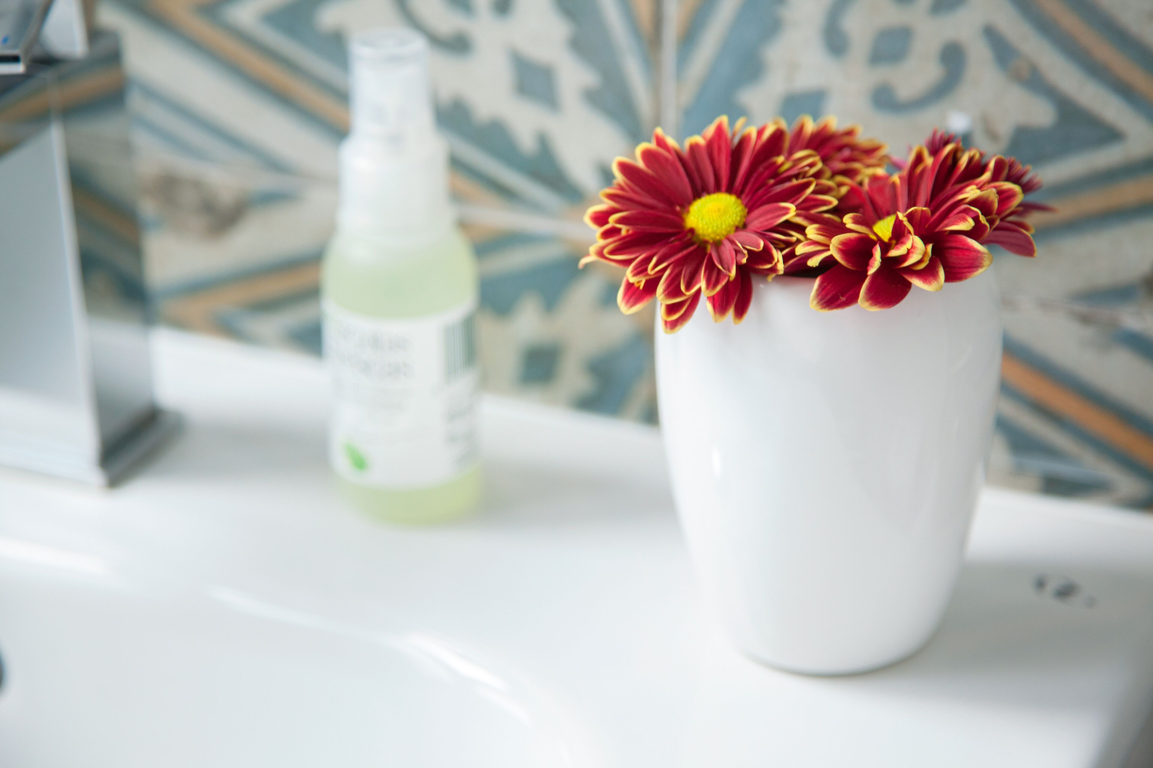A white vase with red and yellow flowers on a white countertop.