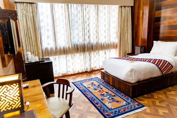 A hotel room with a bed, a desk, a chair, a TV, and a window with curtains.