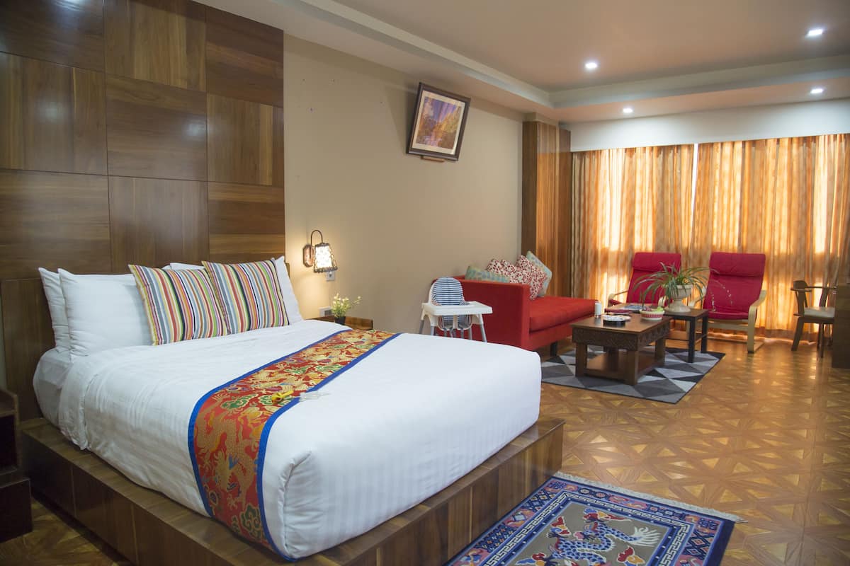 A hotel room with a large bed, a red armchair, a small table, and a view of the outside through curtains.