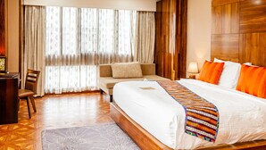 A hotel room with a large bed, a sofa, a desk, and a window with curtains. - Tara Phendeyling Hotel (Thimphu)