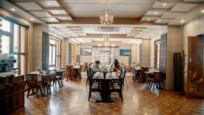 A spacious dining area with wooden flooring, multiple dining tables, and chairs. - Tara Phendeyling Hotel (Thimphu)