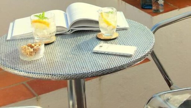 A round metal table with an open book, two glasses of a beverage, and a small container of nuts.