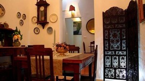 A dining area with a wooden table, chairs, a vase of flowers, and a wall clock.