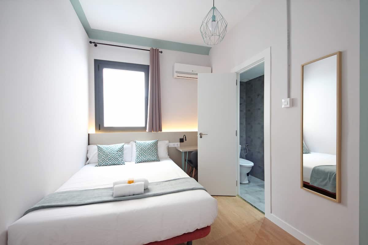 Une chambre d’hôtel moderne avec un grand lit, une table de chevet, un miroir et une vue sur la salle de bain.