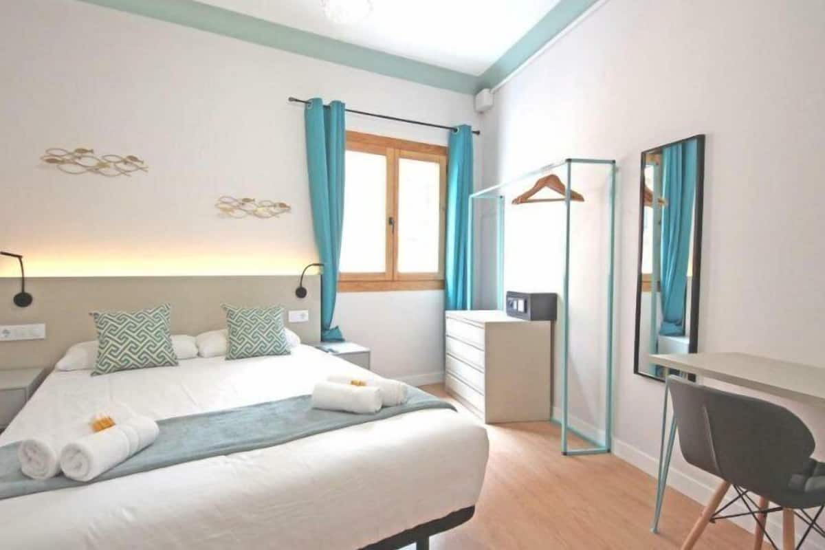 Une chambre d’hôtel moderne comprenant un lit, une table de chevet, une commode, un miroir et une chaise.