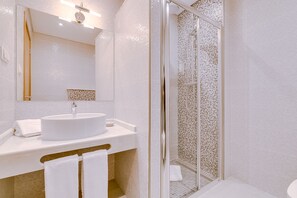 A modern bathroom with a round sink, a glass shower enclosure, and a tiled wall with a mosaic pattern. - Apartamentos Sol e Ria (Olhao)