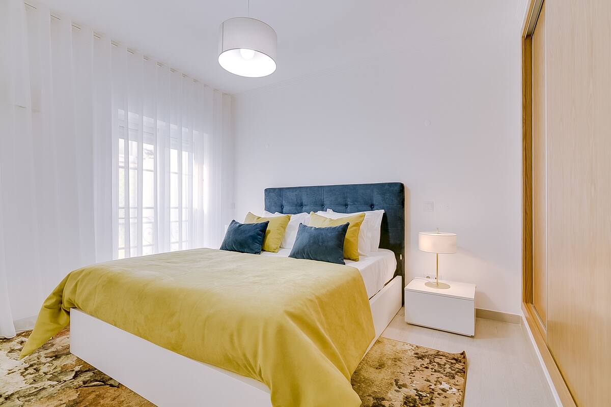 A bedroom with a bed, bedside table, lamp, and a window with curtains.