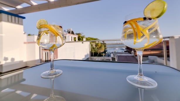 Zwei Gläser mit einem klaren Getränk und Zitronenscheiben auf einem Glastisch unter einer weißen Pergola.