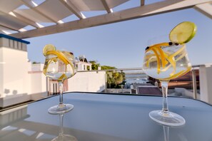 Two glasses of a clear beverage with lemon slices on a glass table under a white pergola. - Apartamentos Sol e Ria (Olhao)