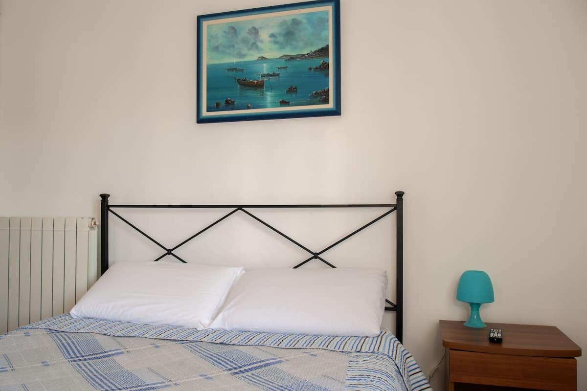 Een slaapkamer met een bed, een nachtkastje met een lamp en een schilderij aan de muur.