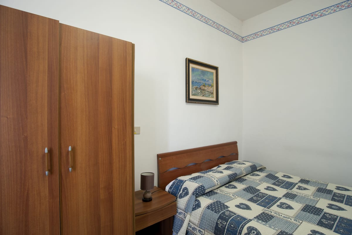 Een slaapkamer met een houten garderobe, een nachtkastje met een lamp en een bed met een bedovertrek met dessin.
