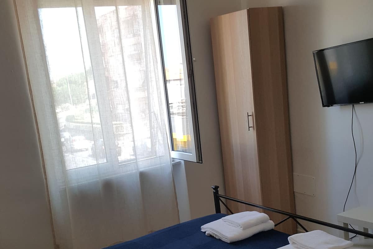 Een slaapkamer met een bed, een kledingkast, een televisie en een raam met gordijnen.