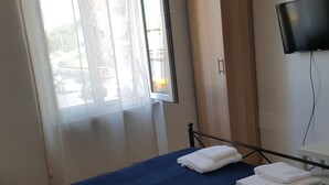 A bedroom with a bed, a wardrobe, a television, and a window with curtains.