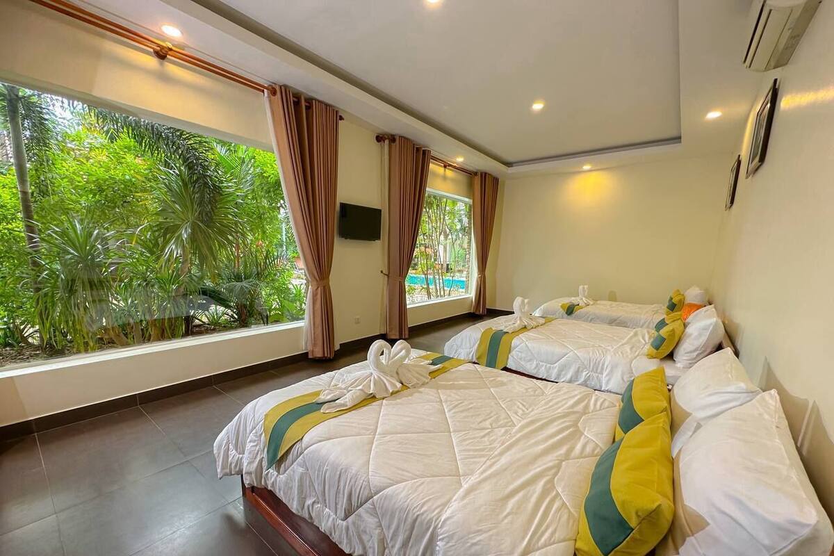 Una camera d'albergo con due letti, ampie finestre con tende e vista sul verde.