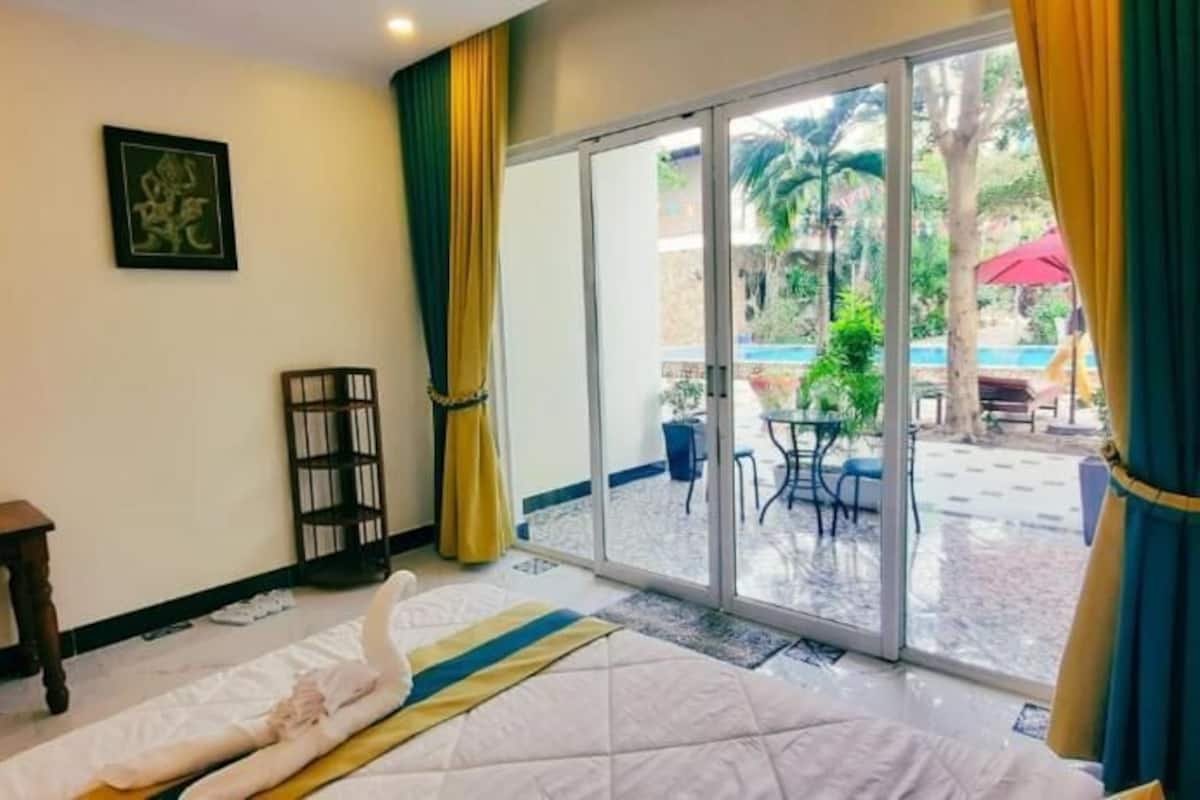 Una camera d'albergo con un letto, una scrivania, una sedia, una televisione e una porta-finestra scorrevole che dà su uno spazio esterno con tavolo e sedie.