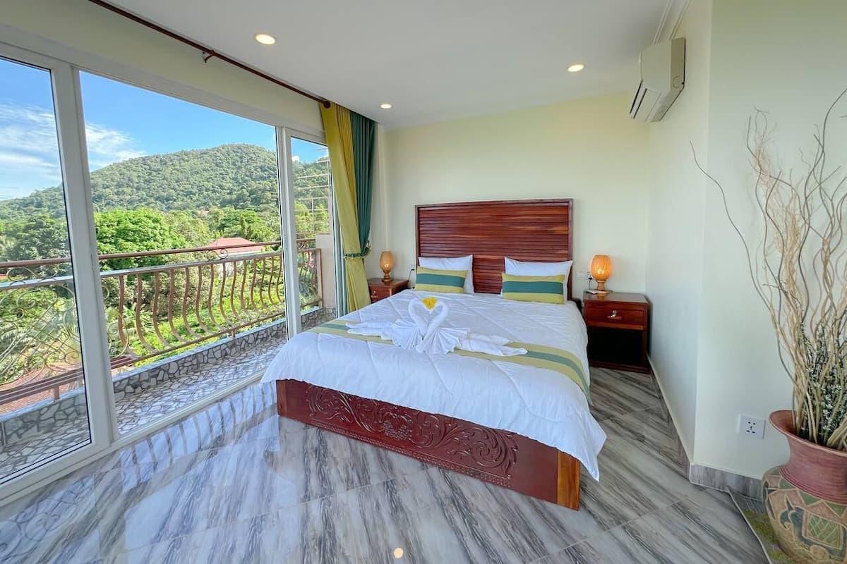 Un letto grande con testiera in legno, un balcone con ringhiera e vista su un paesaggio verde.