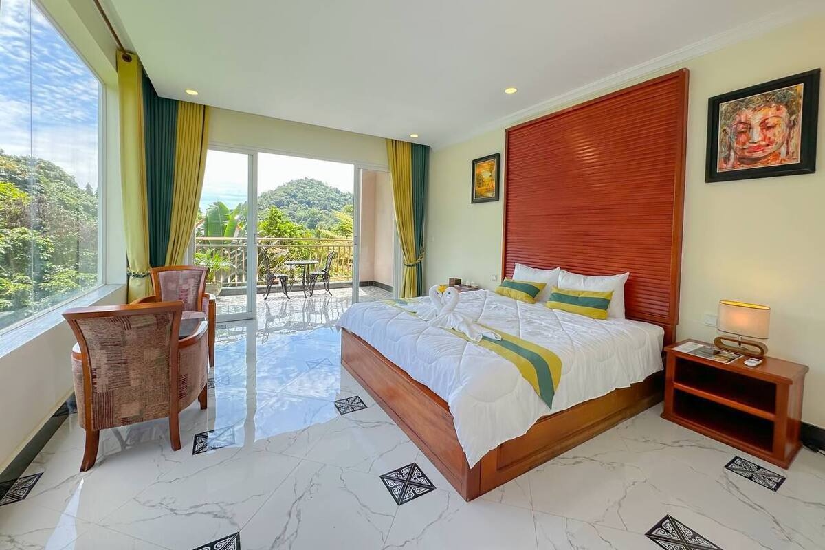 Un'ampia camera da letto con un grande letto, un balcone con zona pranzo e vista sul verde.