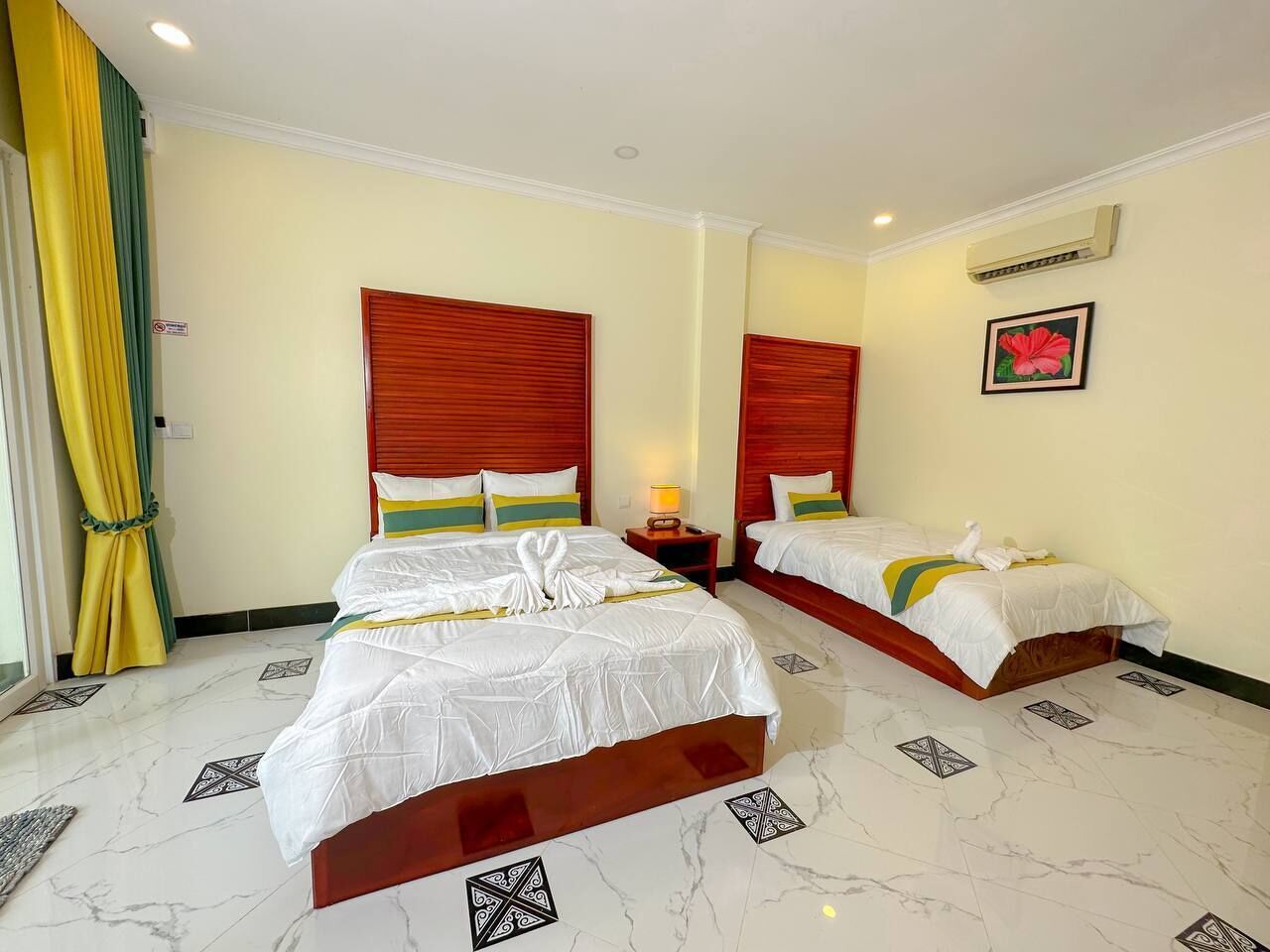 A hotel room with two beds, a nightstand, a lamp, and a window with curtains.
