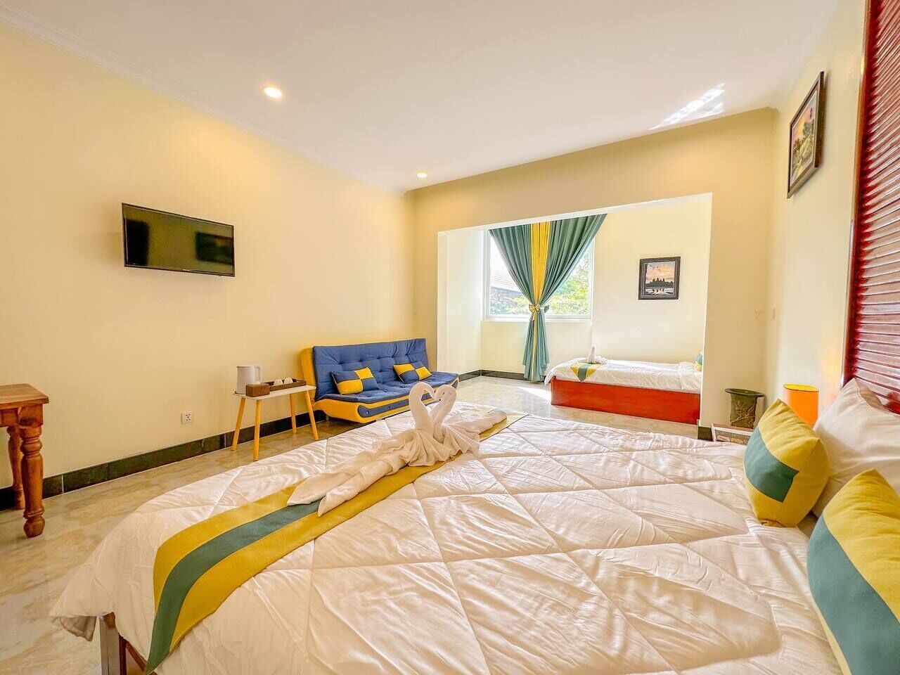 Una habitación de hotel con una cama grande, un sofá, una mesita pequeña y un televisor montado en la pared.