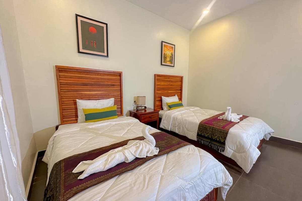 Camera d'albergo con due letti, testiere in legno, biancheria bianca e un quadro appeso al muro.