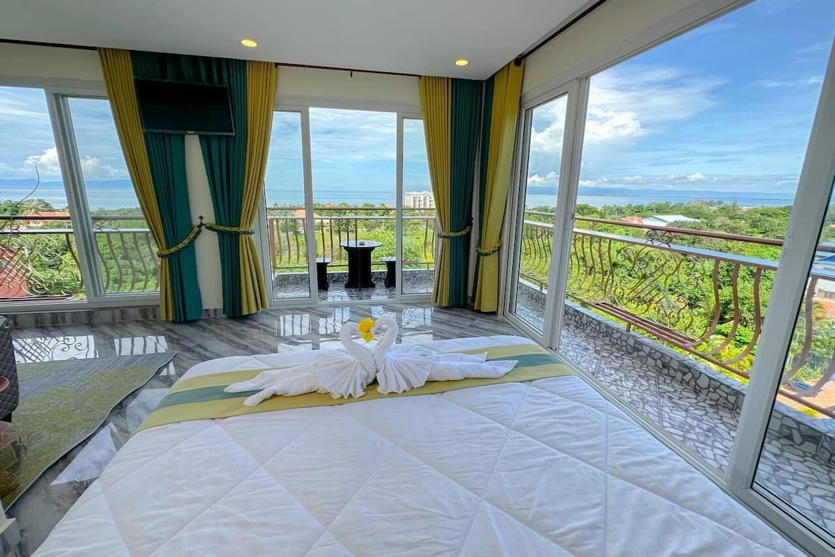 Una camera d'albergo con un letto grande, un balcone vista mare e un'area ristorazione con tavolo e sedie.