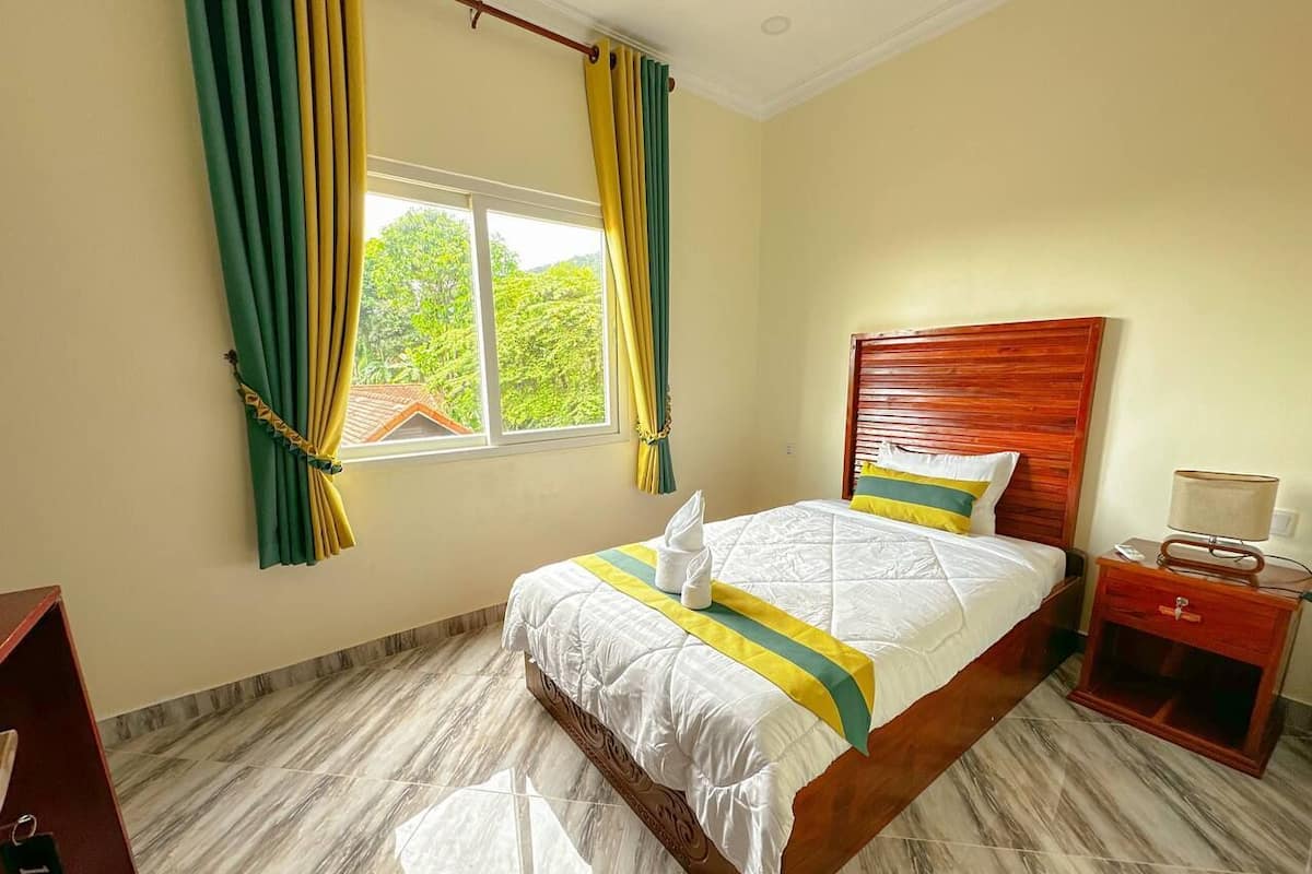 Una camera d'albergo con un letto, una testiera in legno, un comodino e una finestra con tende.