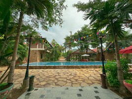Zona de piscina con suelo de piedra, rodeada de palmeras y plantas en macetas.